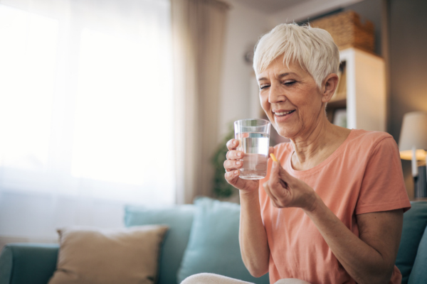 Woman sitting on a couch, about to take a prescription pill with a glass of water