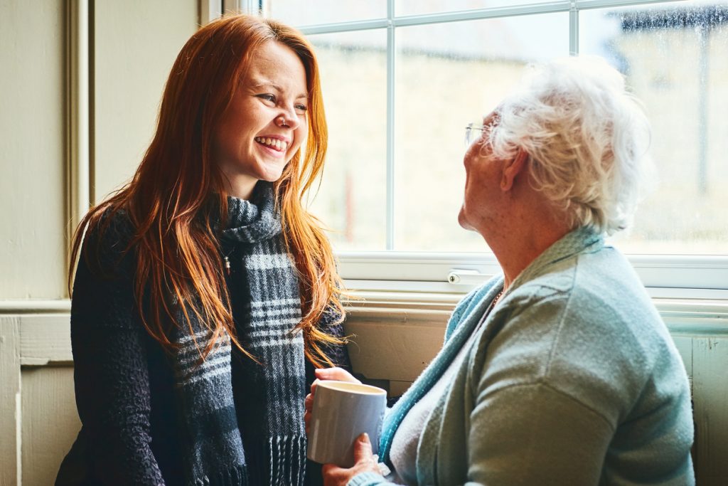 Photograph of a young woman talking with her mother at home and smiling