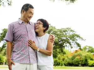 Photo of a man and woman walking happily in the park with arms around each other, looking at each other